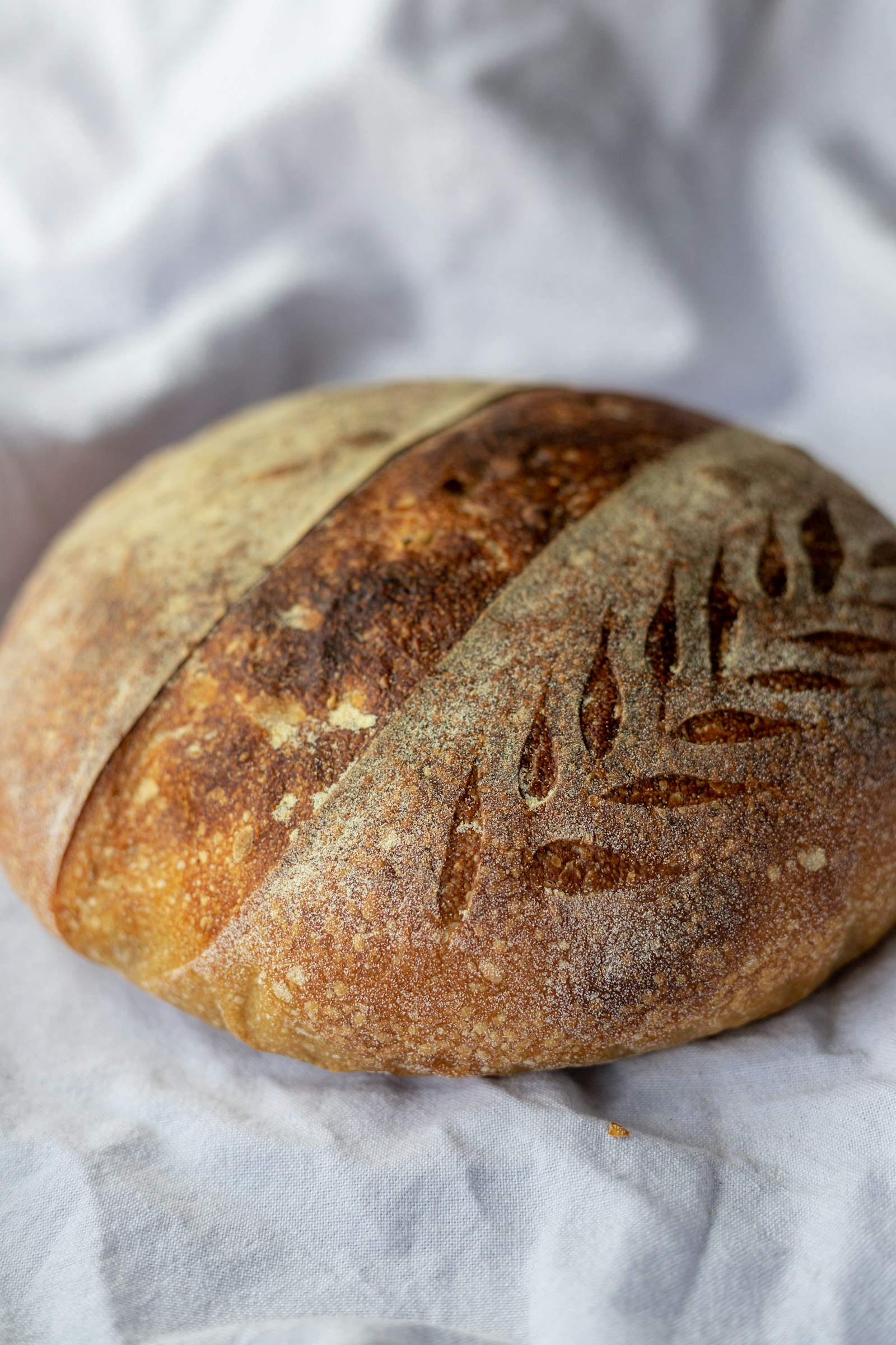 A scored, naturally fermented sourdough loaf resting on white linen